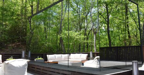 A modern outdoor deck with a mirrored wall, surrounded by lush green trees and a cozy seating area.