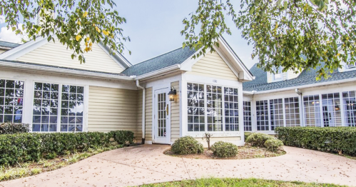 A charming single-story building with large windows, surrounded by greenery and a curved pathway.