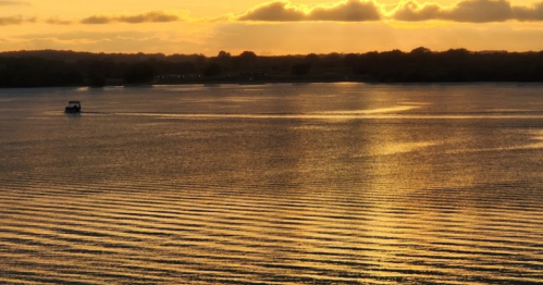 A serene sunset over a calm lake, with gentle ripples and a small boat in the distance.