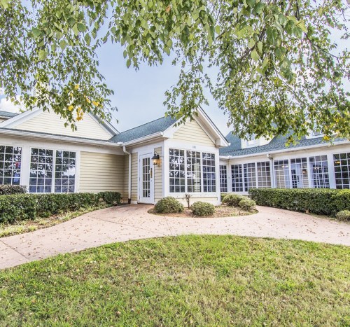 A charming single-story building with large windows, surrounded by greenery and a curved pathway.