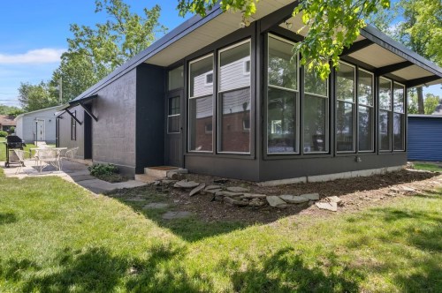 Modern black house with large windows, surrounded by greenery and a small patio area.