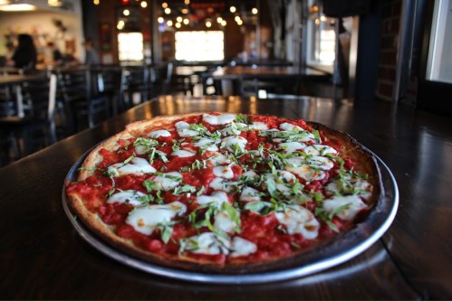 A freshly baked pizza topped with mozzarella and herbs, served on a metal tray in a cozy restaurant setting.