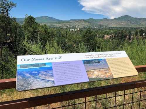 Sign about geological features with mountains and trees in the background, highlighting the area's volcanic history.