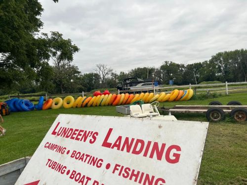 A sign for Lundeen's Landing with colorful tubes and a boat in the background, set in a grassy area.