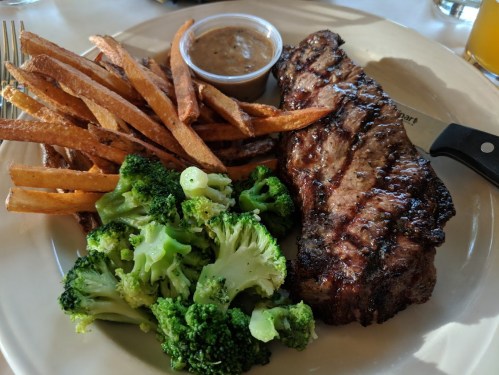 A plate featuring a grilled steak, broccoli, and sweet potato fries with a side of dipping sauce.