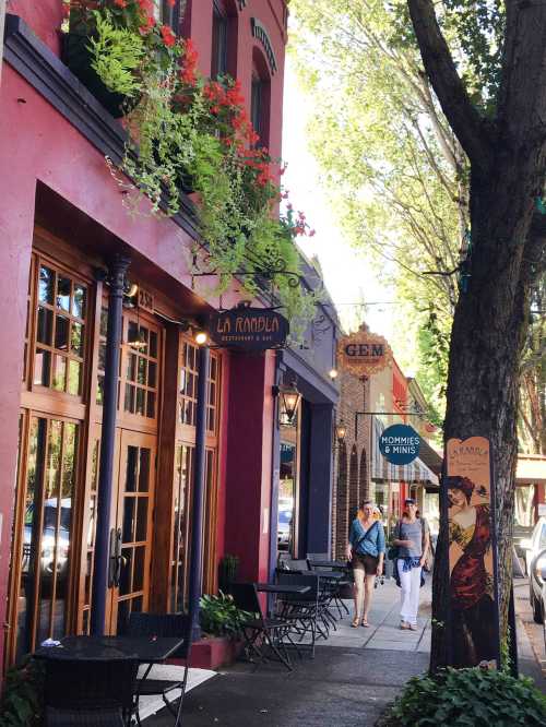 A vibrant street scene with colorful buildings, outdoor seating, and people walking by under sunny skies.