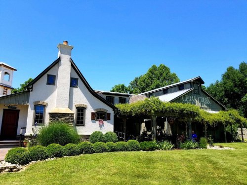 A charming building with a sloped roof, surrounded by lush greenery and a manicured lawn under a clear blue sky.