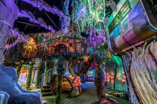A whimsical indoor space with colorful lights, trees, and a multi-level structure resembling a fantasy forest.