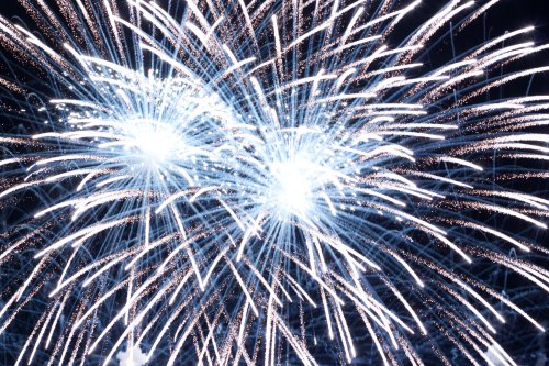 Bright white fireworks burst against a dark sky, creating a dazzling display of light and sparks.