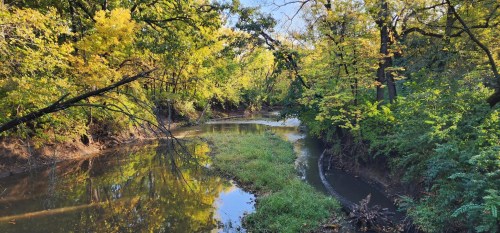 A serene river winding through lush greenery and vibrant autumn trees under a clear blue sky.