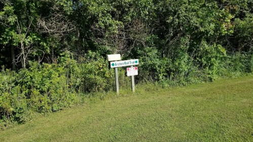 Sign for the Archers Rail Trail, surrounded by greenery and grass.