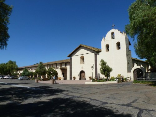 A historic building with a bell tower and cross, surrounded by trees and a clear blue sky.