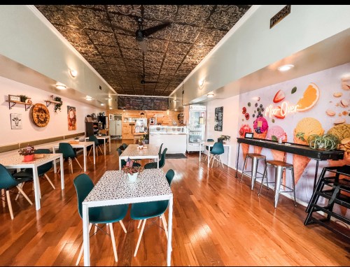 Bright ice cream shop interior with wooden floors, tables, and a colorful wall mural of ice cream cones.