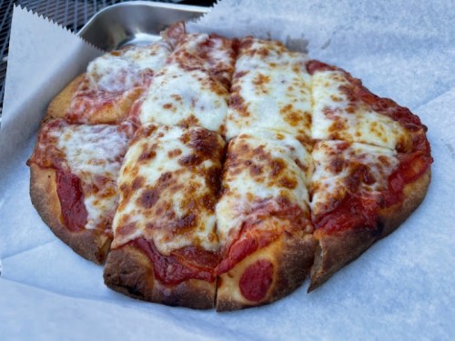 A freshly baked pizza with melted cheese and tomato sauce, cut into slices on a white paper-lined tray.