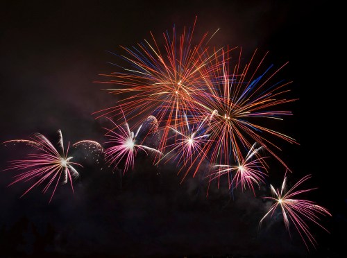 Colorful fireworks burst in the night sky, creating vibrant patterns of red, blue, and white against a dark background.
