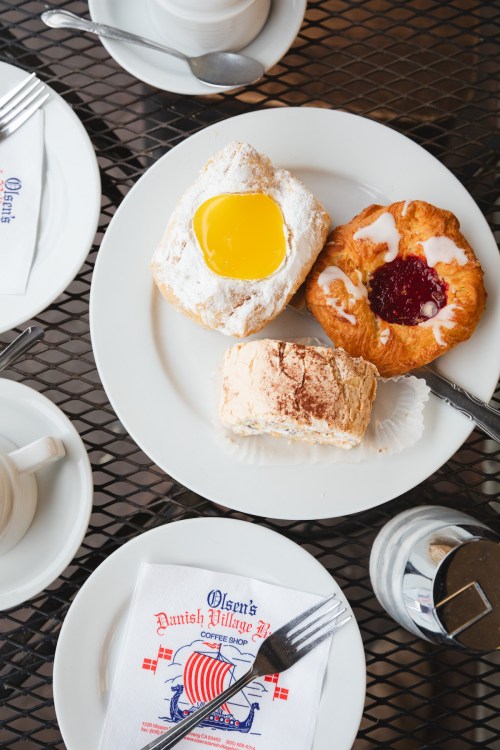 A plate with three pastries: a danish with yellow filling, a fruit-filled pastry, and a cream-filled pastry, on a table.
