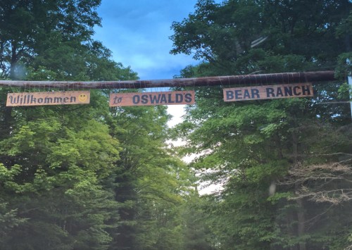 A wooden sign reading "Willkommen to Oswald's Bear Ranch" hangs over a tree-lined entrance.