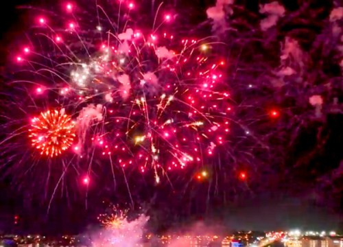 Colorful fireworks explode in the night sky, creating a vibrant display of pink, white, and gold against a dark backdrop.