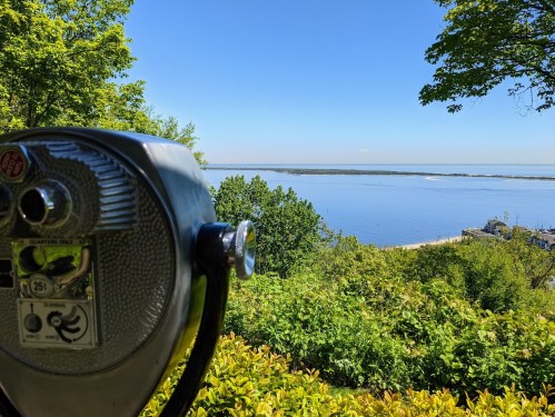 A scenic view of a calm lake from a lookout, featuring a coin-operated binocular viewer in the foreground.