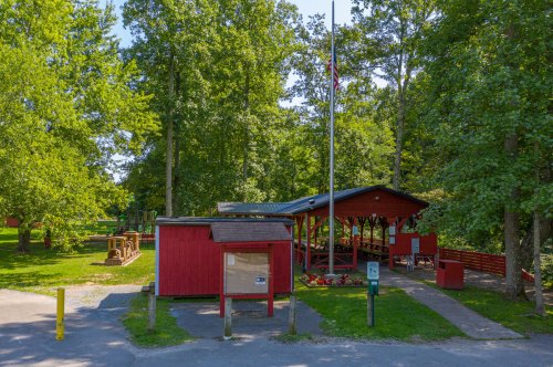 A red building and pavilion surrounded by trees in a park, with a playground visible in the background.