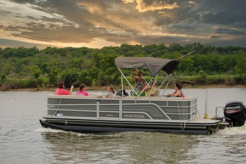 A group of people enjoying a boat ride on a lake at sunset, with lush greenery in the background.