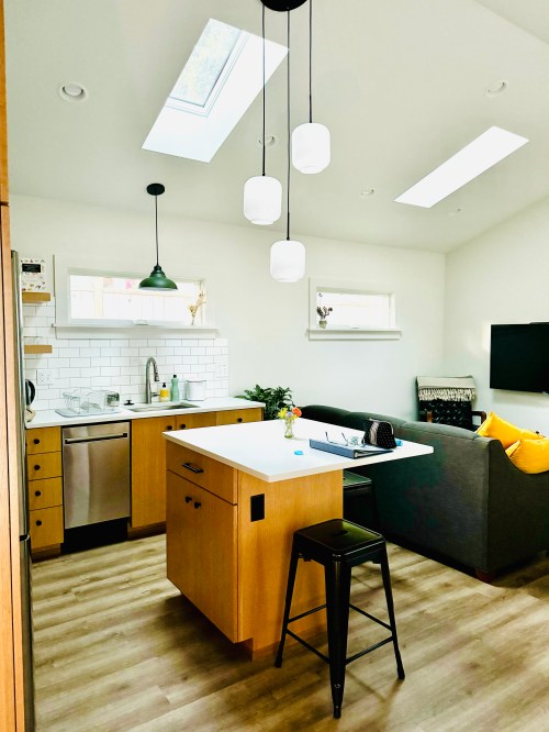 Bright, modern kitchen with skylights, wooden cabinets, a dining island, and a cozy living area with a sofa and TV.