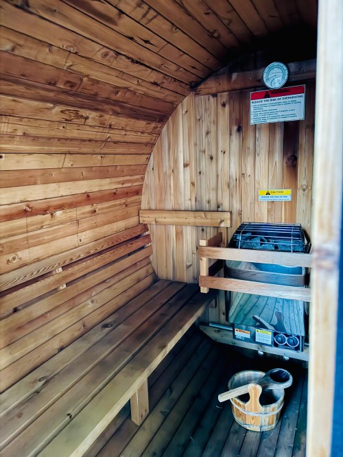 Interior of a wooden sauna with benches, a stove, and a thermometer on the wall.