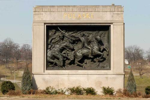 A stone monument featuring a relief sculpture of two horsemen in battle, with "PULASKI" inscribed above.