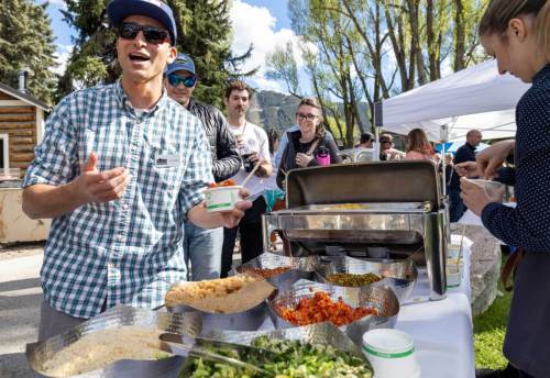 A man in sunglasses serves food at an outdoor event, with people enjoying the meal in the background.