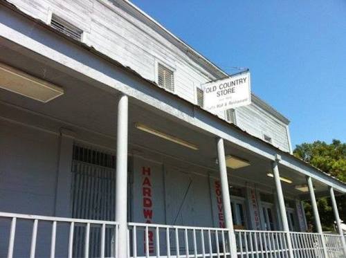 Exterior of an old country store with a sign, featuring a porch and windows under a clear blue sky.