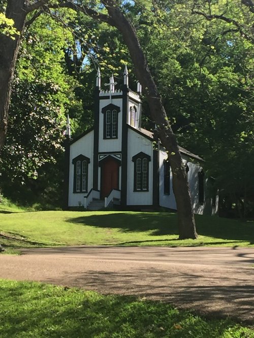 A small, black and white church with a red door, surrounded by lush green trees and grass.