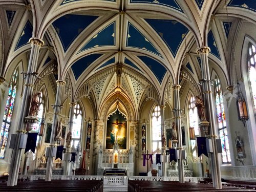 Interior of a grand church featuring intricate arches, stained glass windows, and a central altar with religious artwork.