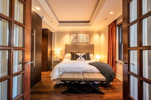 Cozy bedroom with a large bed, decorative headboard, warm lighting, and stylish furnishings.