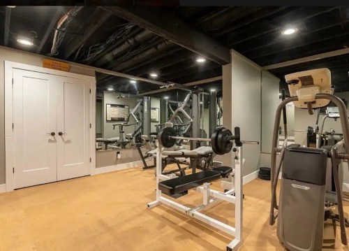 A home gym featuring a weight bench, barbell, mirrors, and exercise equipment in a well-lit basement space.