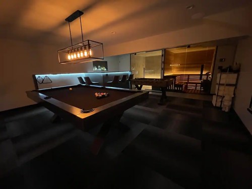 A dimly lit game room featuring a pool table, modern lighting, and seating areas.