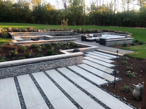 A landscaped backyard featuring stone pathways, garden beds, and a seating area with modern furniture.