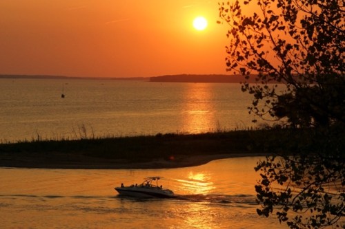 A boat glides across a tranquil lake at sunset, with vibrant orange and yellow hues reflecting on the water.