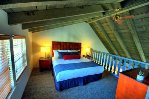 Cozy attic bedroom with sloped wooden ceiling, a queen bed, bedside tables, and warm lighting.