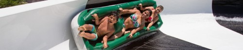 Three children enjoying a water slide, laughing as they ride in a green inflatable raft.