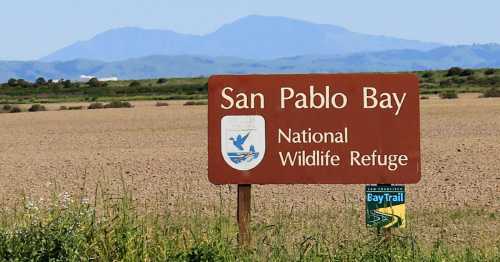 Sign for San Pablo Bay National Wildlife Refuge with mountains in the background and a BayTrail marker nearby.