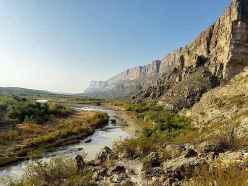 A serene landscape featuring a winding river surrounded by rocky cliffs and lush vegetation under a clear blue sky.
