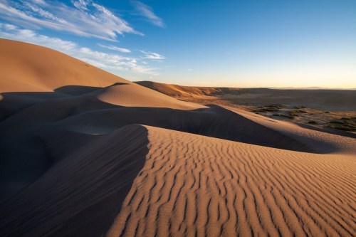 A serene desert landscape with rolling sand dunes under a clear blue sky and soft sunlight.