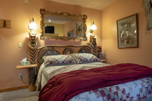 Cozy bedroom featuring a carved wooden bed, decorative mirror, and warm lighting against a peach-colored wall.