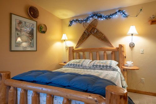 Cozy bedroom with a wooden bed, blue bedding, wall decor, and soft lighting from lamps and fairy lights.