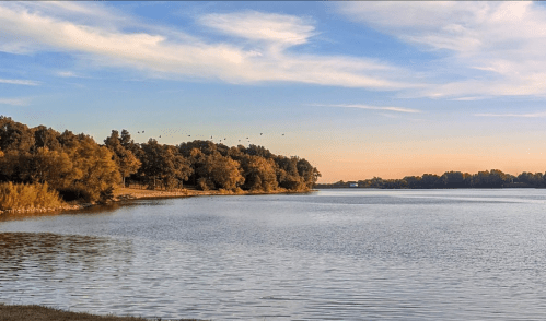 A serene river scene at sunset, with trees lining the shore and birds flying in the sky.