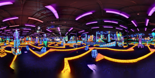 A vibrant, neon-lit mini-golf course featuring Halloween-themed decorations and glowing pathways.