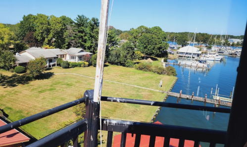 View from a balcony overlooking a marina, grassy area, and nearby houses surrounded by trees.