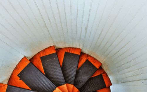 A spiral staircase with wooden steps and a white, textured wall surrounding it.