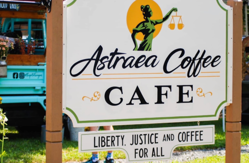Sign for Astraea Coffee Cafe featuring a woman holding scales, with the slogan "Liberty, Justice, and Coffee for All."