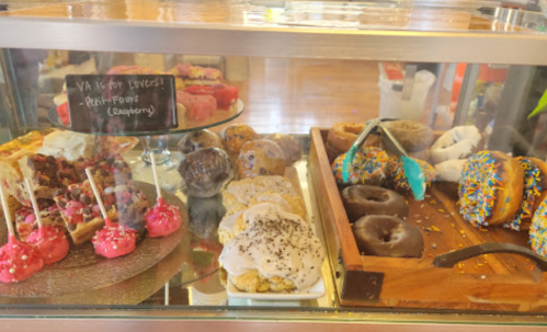 A display case filled with colorful pastries, cookies, and donuts, including raspberry petit fours and decorated donuts.